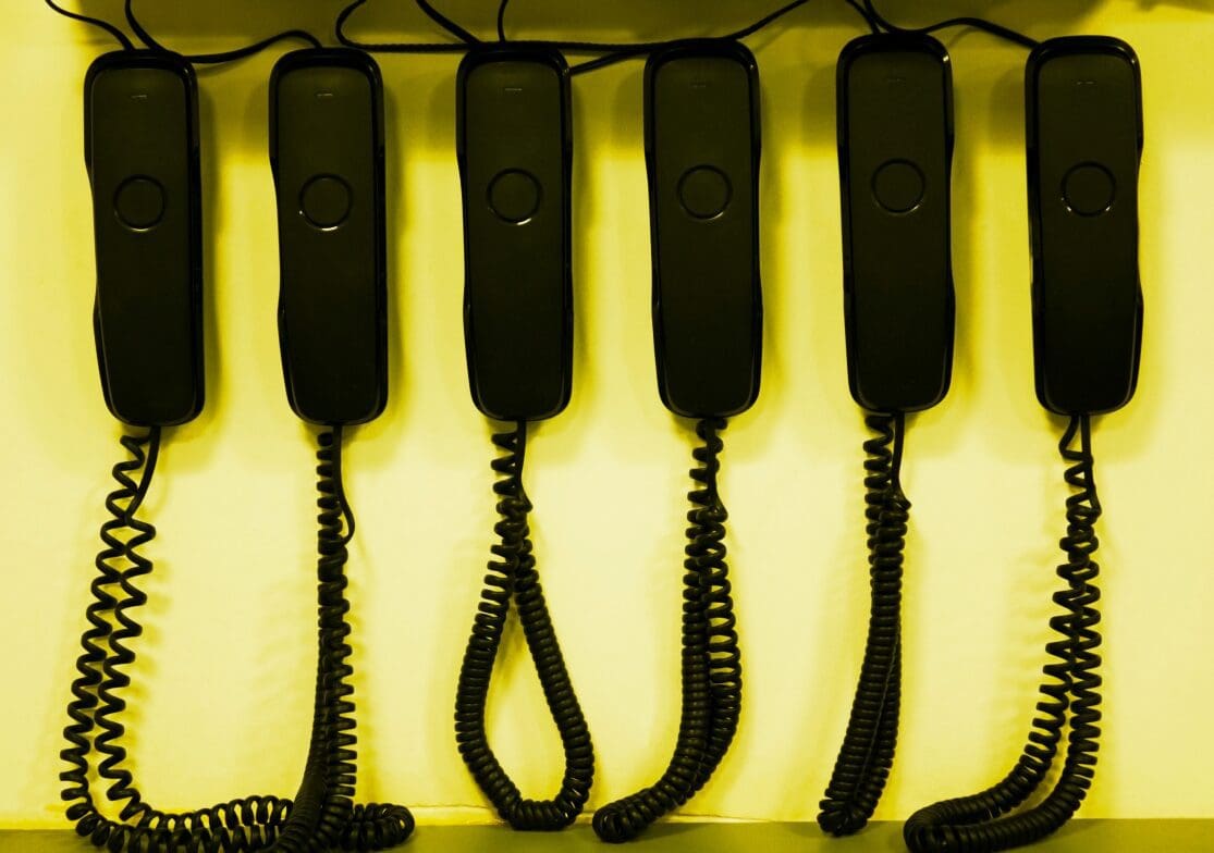 Six black telephone handsets hanging.
